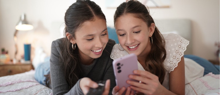Two girls looking at a smartphone together on a family mobile plan