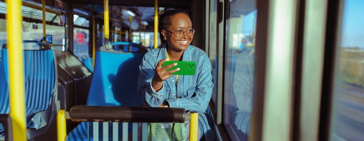 Smiling woman using her smartphone while riding on a bus.