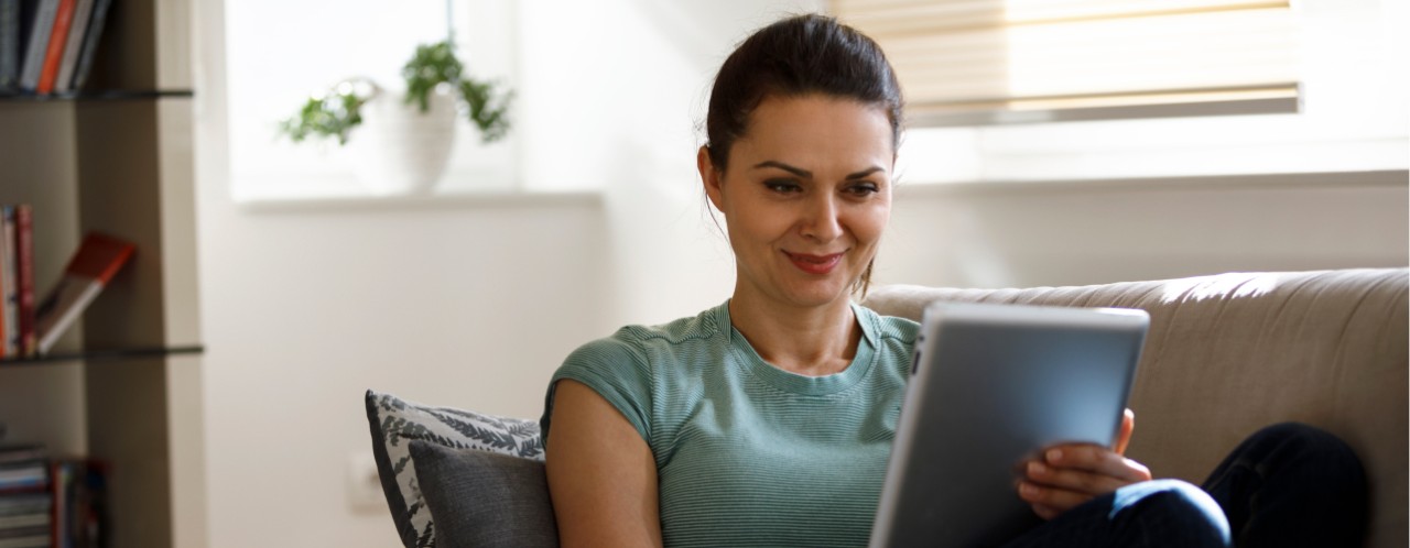Woman smiling while using a tablet on a couch in a bright living room