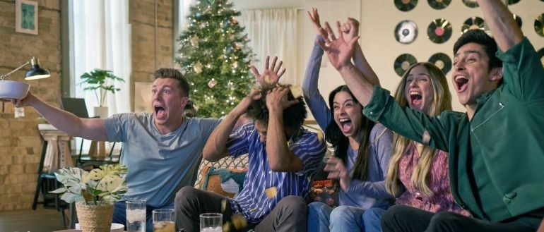 A hand pressing a button on a TV remote in front of a TV.