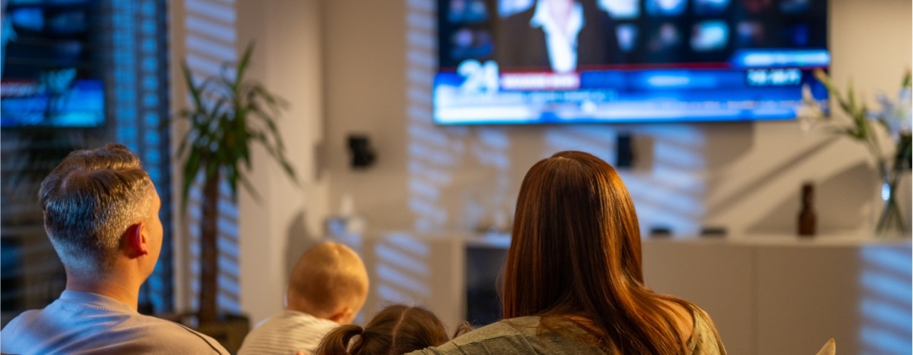 A family of four watching TV in the living room. 