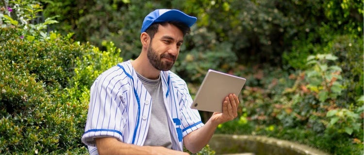 Fanático del béisbol viendo deportes en su tableta, en la naturaleza