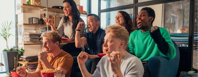Six friends cheering and eating snacks while watching a sports game.