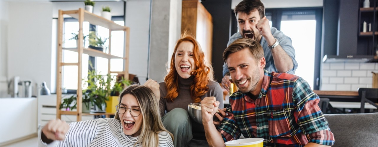 Four people gathered around a couch, cheering.
