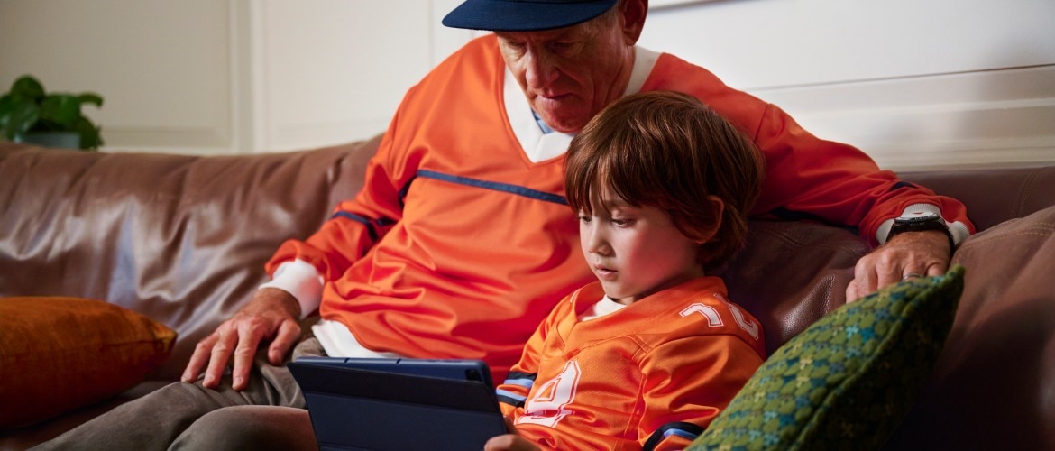A man and boy sitting on a couch together, looking at a tablet. 