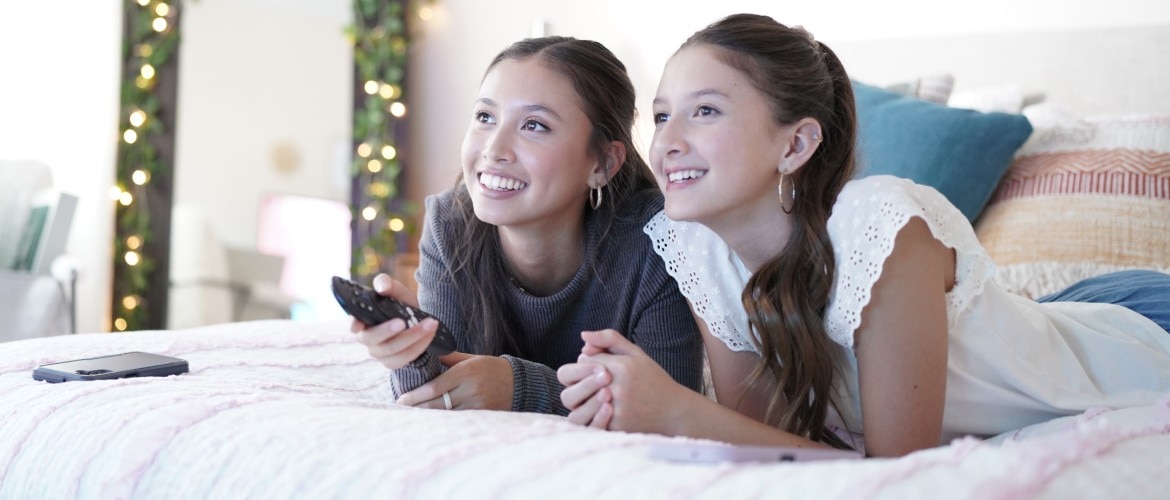 Una mano presionando un botón de control remoto frente a un TV.